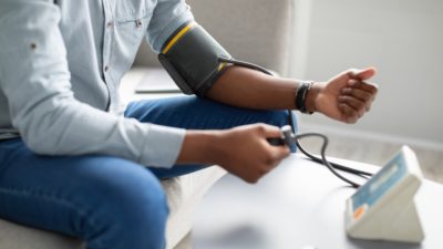 Unrecognizable African Guy Measuring Arterial Pressure Having Hypertension Indoor, Cropped