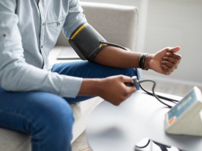 Unrecognizable African Guy Measuring Arterial Pressure Having Hypertension Indoor, Cropped