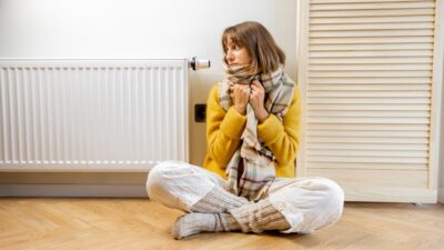 Warmly dressed woman near heater at home