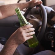 Bottle of beer in a man's hands driving the car during daytime