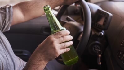 Bottle of beer in a man's hands driving the car during daytime