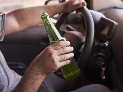 Bottle of beer in a man's hands driving the car during daytime