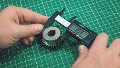 Metal gear measurement process. Factory man, worker measuring steel detail, gear with digital