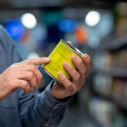 Close-up of person in grocery store examining product label on canned food with focus on details